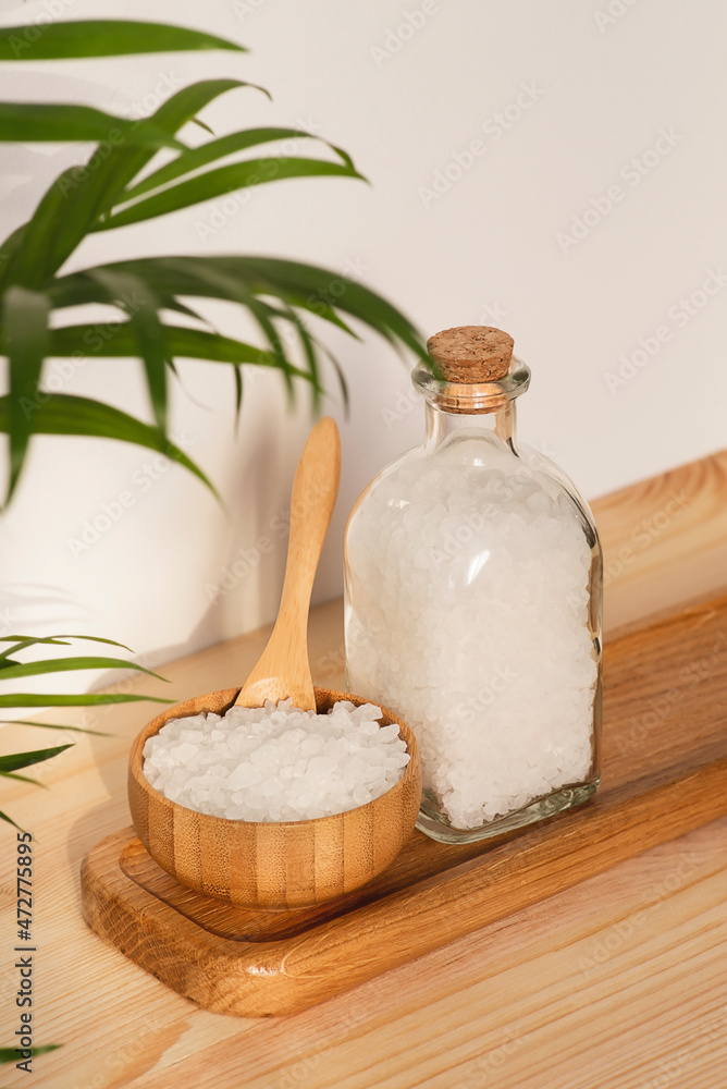 Wooden bowl and bottle filled with white bath sea salt on natural wooden background. Beauty treatment for spa and wellness. Skincare natural cosmetic concept for body care. Wooden bowl and bottle filled with white bath sea salt on natural wooden background. Beauty treatment for spa and wellness. Skincare natural cosmetic concept for body care.