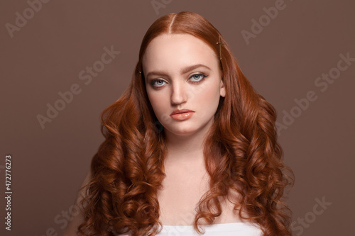 Nice perfect young woman redhead model looking at camera on brown background