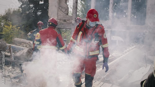 Male paramedic in mask walking on remains of destructed building near colleagues during rescue mission after cataclysm