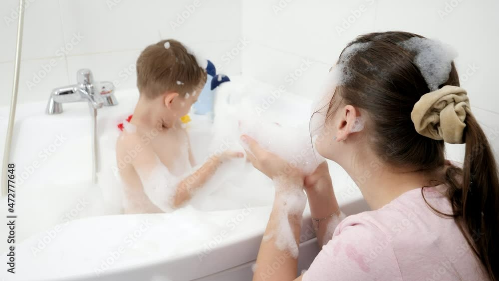 Funny mother with son splashing water in bath and throwing soap suds. Concept of hygine, children development and fun at home Funny mother with son splashing water in bath and throwing soap suds. Concept of hygine, children development and fun at home