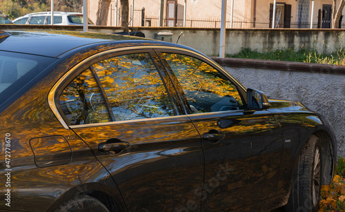 Reflection of yellow autumn leaves in the shiny side and window of the car