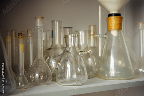 Various glass flasks on the shelf, close-up. Equipment for experiments in the school laboratory. Used empty test tubes.