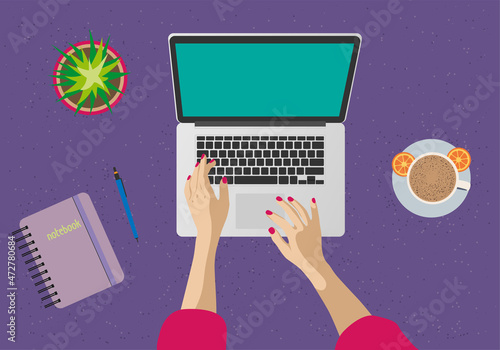 A woman is working behind a computer screen. Top view of the desktop, monitor, keyboard, laptop, notepad, pen, flower, hands, coffee