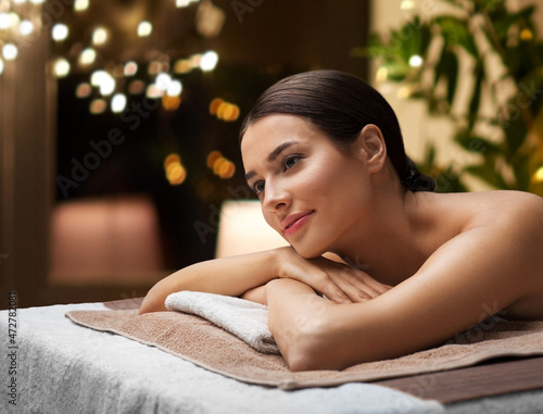 wellness, beauty and relaxation concept - young woman lying at spa or massage parlor over christmas lights on window background