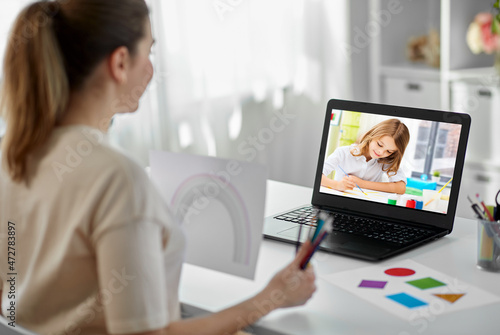 distant education, school and people concept - female teacher with student girl on laptop computer screen and picture of rainbow having online class at home