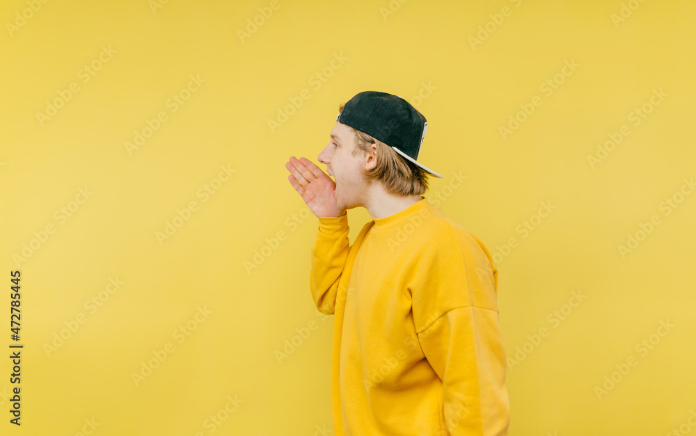 Guy on a yellow background shouts aside in palms on copy space Guy on a yellow background shouts aside in palms on copy space