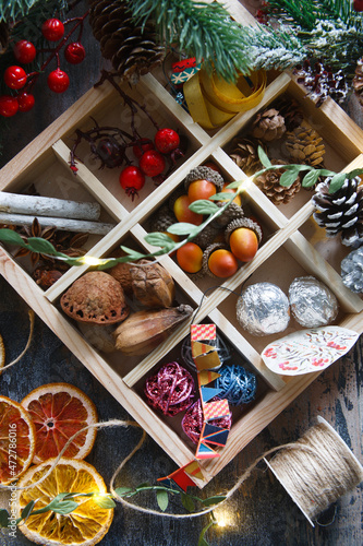 Natural materials for home made garlad - dry orange chips, nuts, arcons, berries, cinnamon sticks and pine cones, eco friendly, on wooden table with lights and fur tree branch, flat lay photo