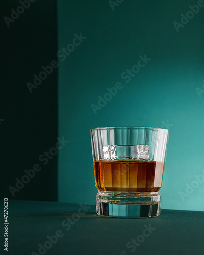 Whiskey with ice in a transparent glass on a green background