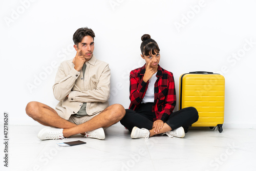 Young mixed race travelers couple sitting on the floor isolated on white background looking to the front