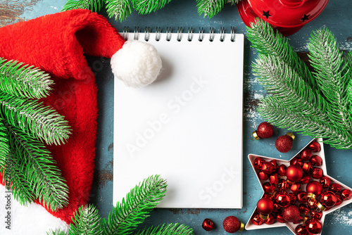 Christmas or New Year's blue festive background with an open blank notebook, fir branches and red decorations. A checklist or a letter to Santa. Top view with copy space