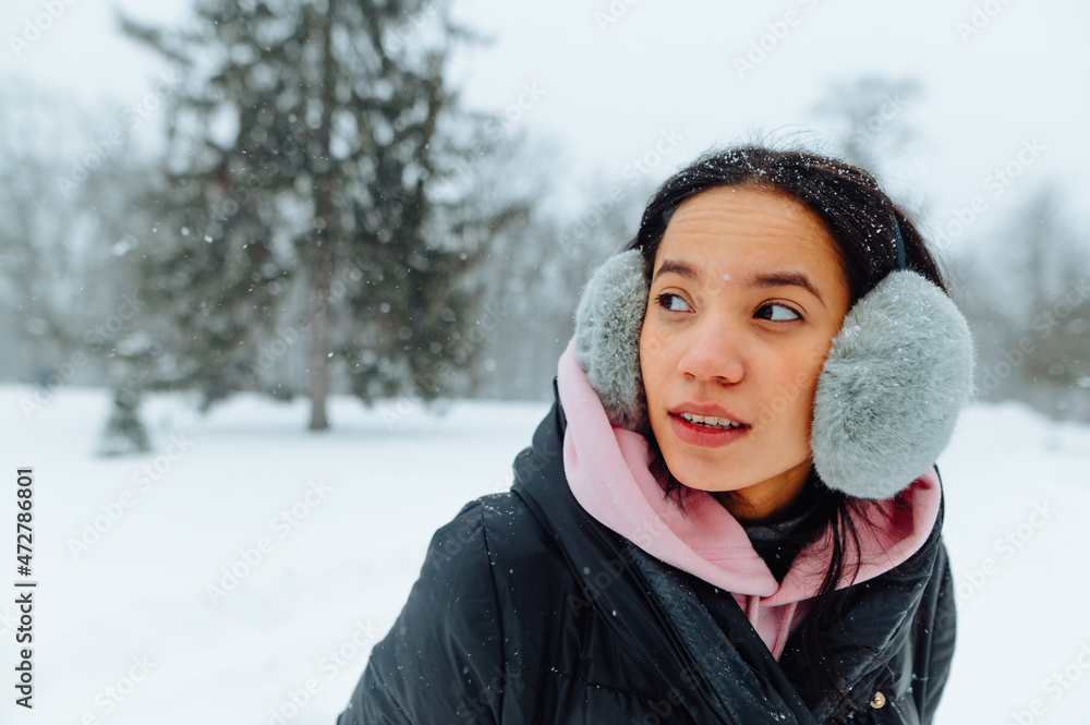 Portrait of a positive Hispanic woman walking in a frosty park on a snowy winter day and looking away with a cheerful face. Portrait of a positive Hispanic woman walking in a frosty park on a snowy winter day and looking away with a cheerful face.