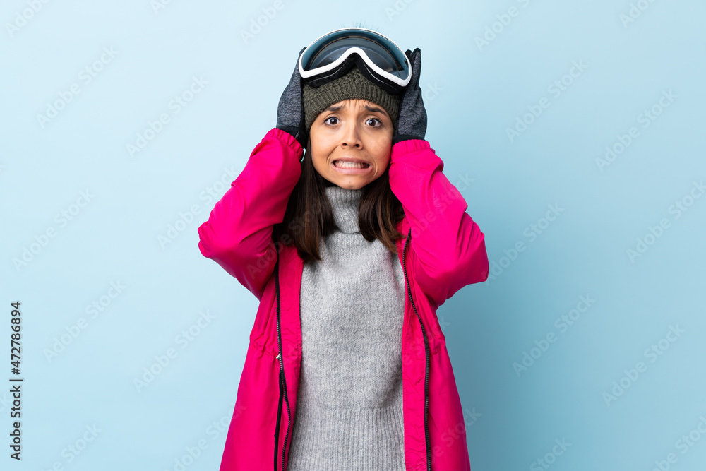 Mixed race skier girl with snowboarding glasses over isolated blue background doing nervous gesture. Mixed race skier girl with snowboarding glasses over isolated blue background doing nervous gesture.
