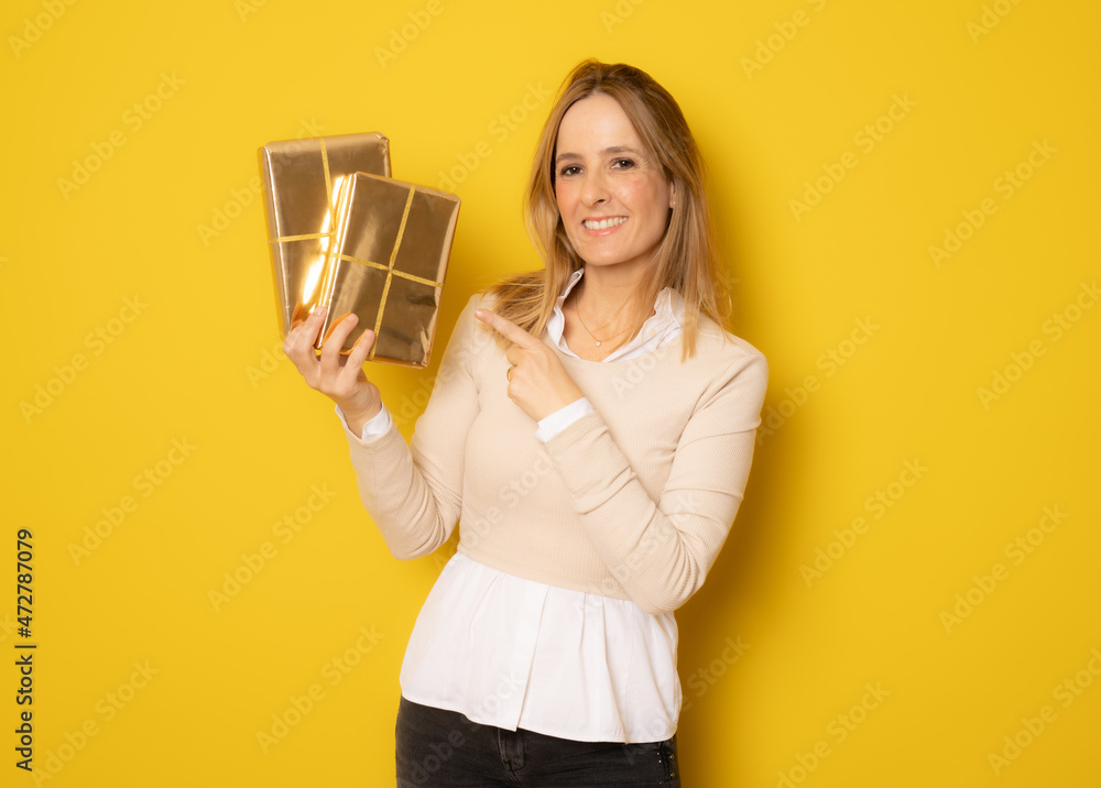 Happy beautiful woman showing gift boxes standing isolated over yellow background. Happy beautiful woman showing gift boxes standing isolated over yellow background.