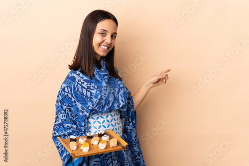 Woman wearing kimono and holding sushi over isolated background pointing back