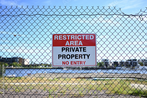 A restricted area sign, signalling that beyond the fence is private property and that no entry is permitted, on a fence. The undeveloped waterfront land can be seen in the background photo