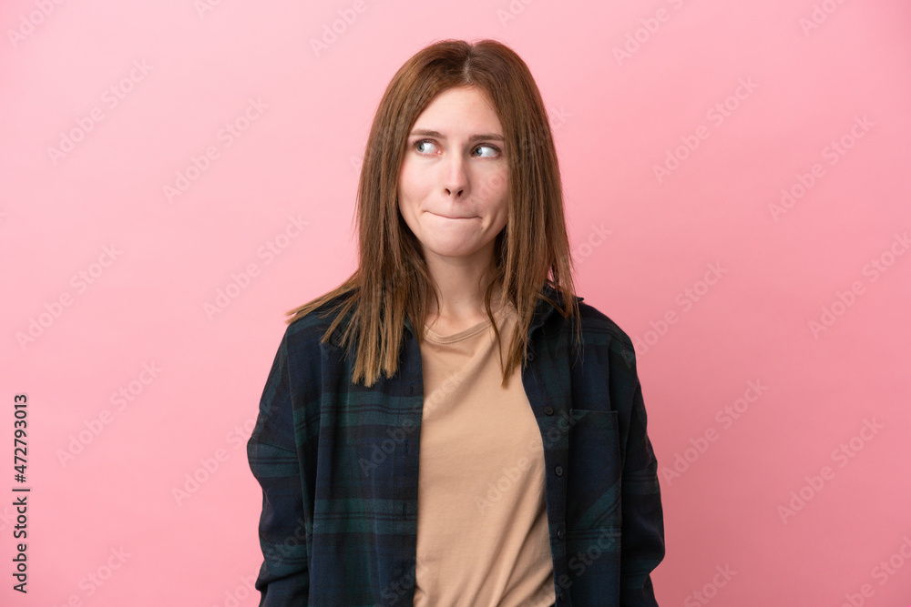 Fototapeta premium Young English woman isolated on pink background having doubts while looking up