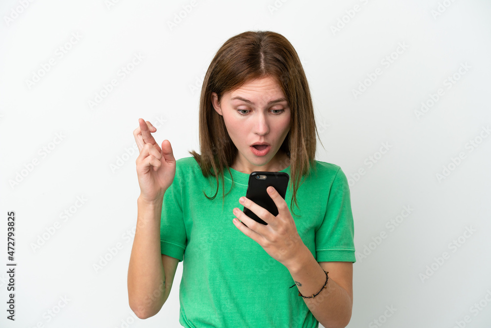 Young English woman isolated on white background using mobile phone with fingers crossing Young English woman isolated on white background using mobile phone with fingers crossing