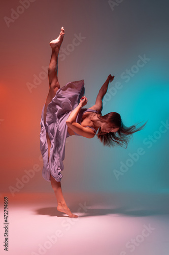 Fototapeta Naklejka Na Ścianę i Meble -  Dynamic portrait of young flexible contemp dancer dancing isolated on gradient blue orange background in neon.