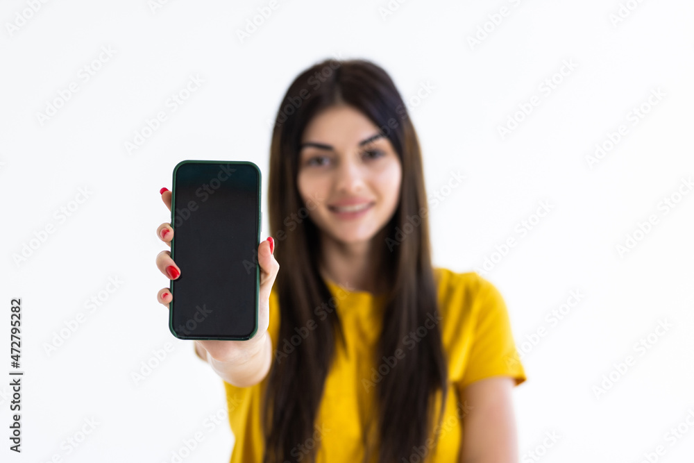 Happy beautiful young woman holding blank screen mobile phone and pointing finger over white background Happy beautiful young woman holding blank screen mobile phone and pointing finger over white background