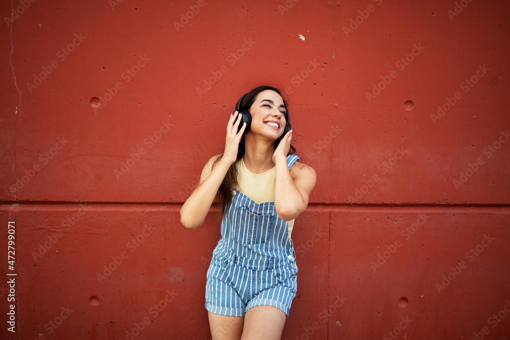 Young happy woman listening to music outdoors. Positive hipster girl with headphones enjoying in sunny day..