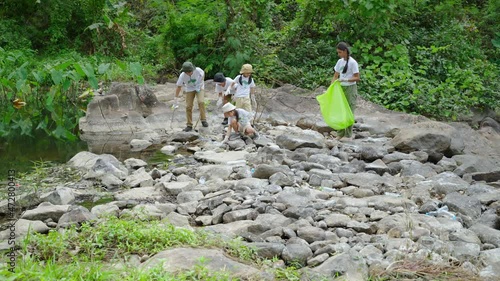 Voluntee Asian and children are collecting plastic bottles that flow through the stream into garbage bags to reduce global warming and environmental pollution. Volunteering and recycling concept.
 photo