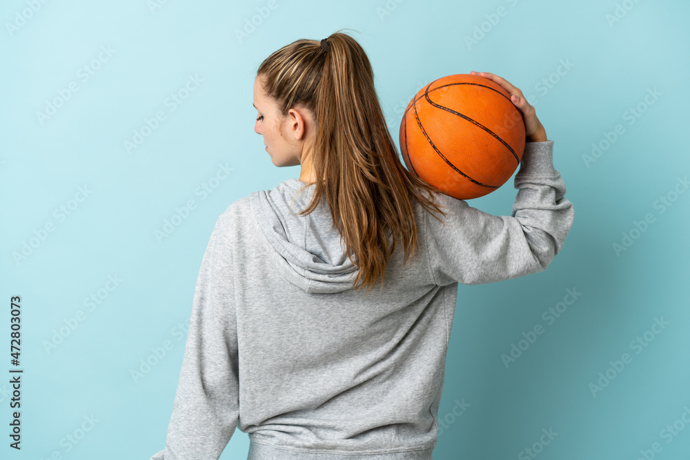 Young caucasian woman isolated on blue background playing basketball in back position