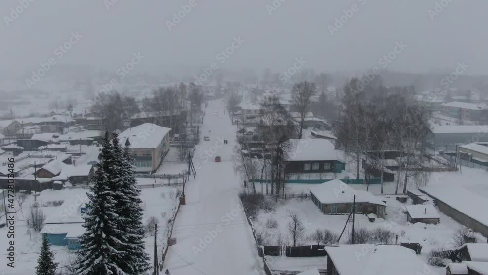 Aerial shot in movement over road to the right of snowed town when strong snow-storm in evening