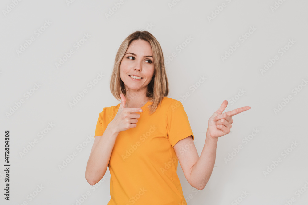 Positive young woman in yellow t-shirt pointing her finger to the side. On white background. Hand gestures Positive young woman in yellow t-shirt pointing her finger to the side. On white background. Hand gestures