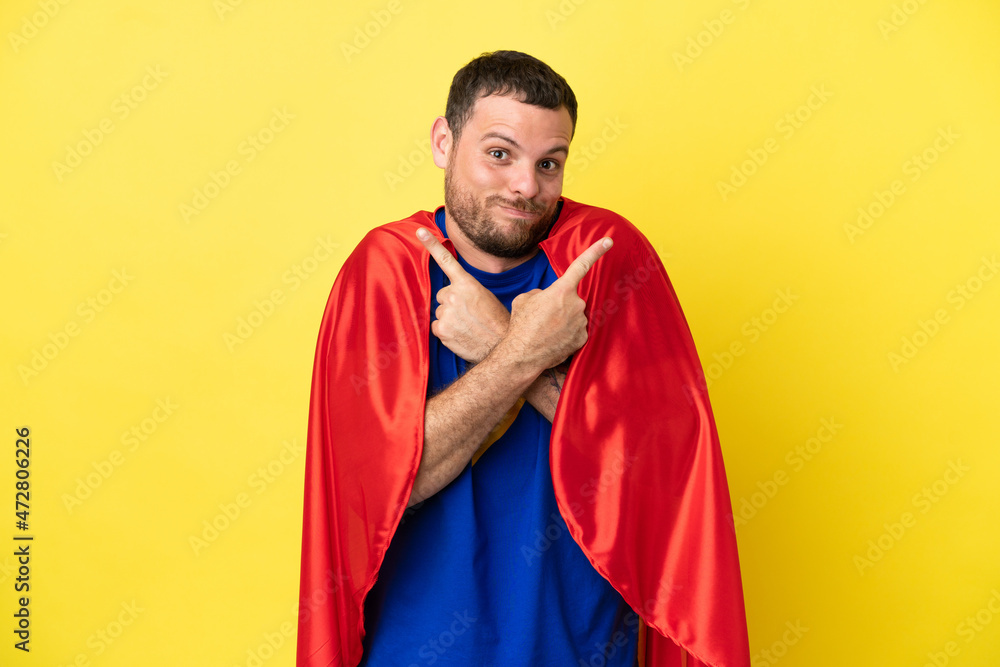 Super Hero Brazilian man isolated on yellow background pointing to the laterals having doubts