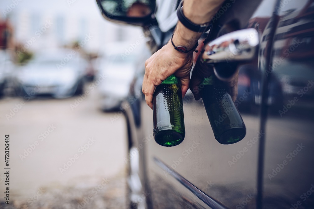Naklejka premium Drunk driver drinking alcohol in car and holding beer bottle