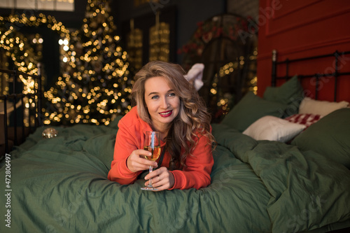 Happy New Year to you. One beautiful young woman with blond hair on the bed at home. Celebrating Christmas with a glass of champagne. New Year party. Christmas Eve. The blonde lies on the bed with a © екатерина лагунова