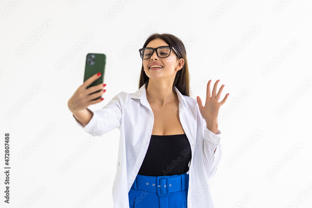 Young woman taking selfie, sending kisses at mobile phone camera, romatnic video call on smarpthone app, standing against white background Young woman taking selfie, sending kisses at mobile phone camera, romatnic video call on smarpthone app, standing against white background