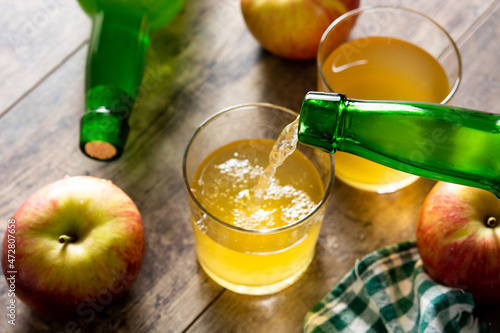 Fotografering Pouring apple cider drink into a glass on wooden rustic table