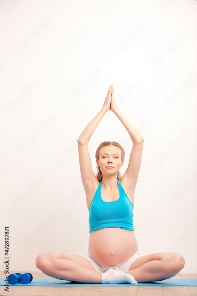 Relaxation for both of them. Beautiful pregnant woman exercising and keeping eyes closed while sitting in lotus position.