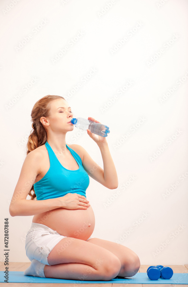 Water is important for me and my baby. Beautiful pregnant woman drinking water while sitting on mat. Water is important for me and my baby. Beautiful pregnant woman drinking water while sitting on mat.
