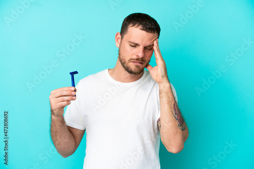 Brazilian man shaving his beard isolated on blue background with headache