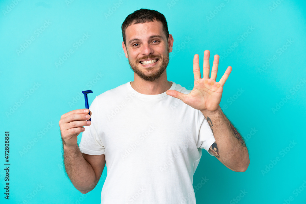 Brazilian man shaving his beard isolated on blue background counting five with fingers Brazilian man shaving his beard isolated on blue background counting five with fingers