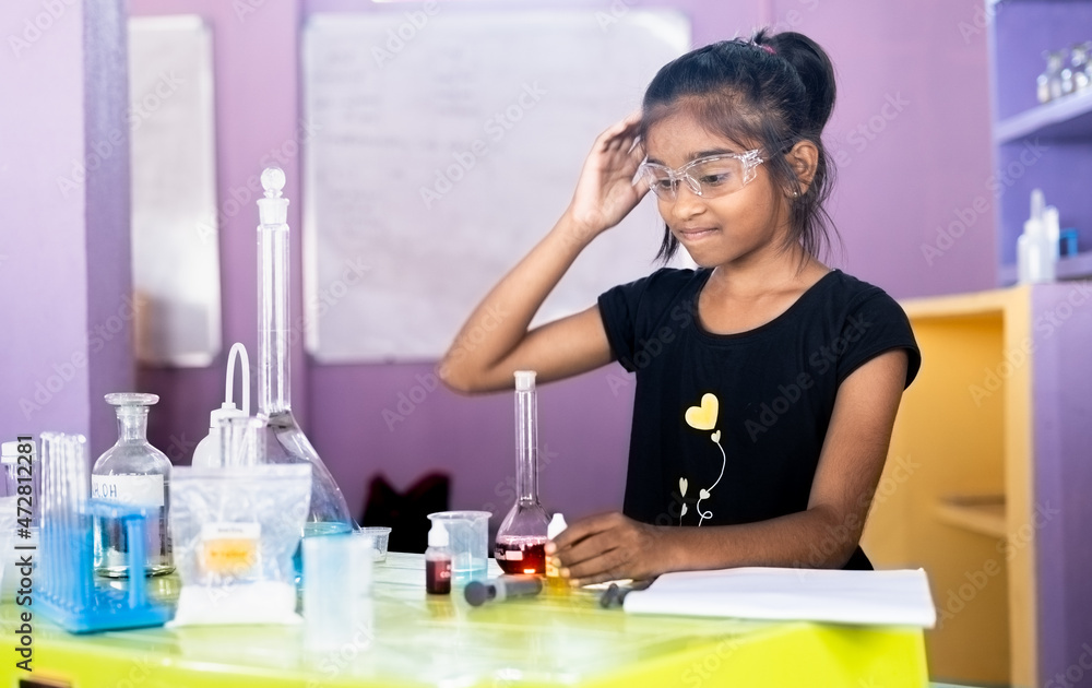 Confused girl kid scratching head by looking lab equipments at chemistry laboratory while making experiment - concept of difficulty in learning at school