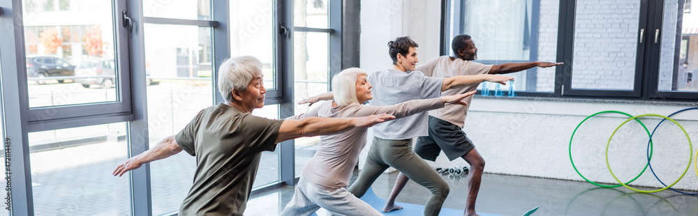 © LIGHTFIELD STUDIOS - Interracial senior people doing warrior pose in sports center, banner.