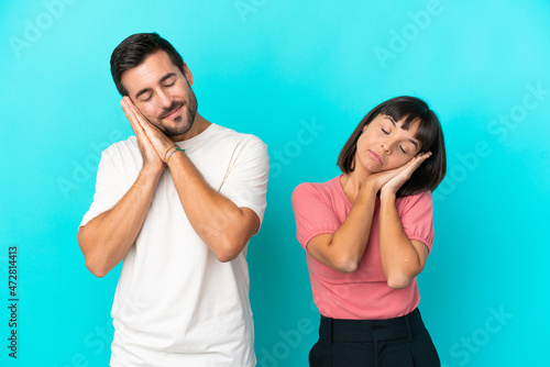 Young couple isolated on blue background making sleep gesture in dorable expression
