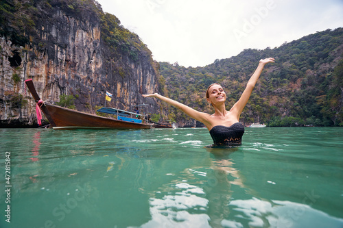 Vacation and happiness. Pretty young woman rising hands up standing on tropical beach with beautiful view in Thailand. © luengo_ua