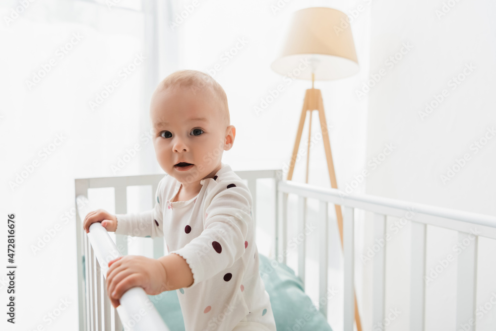 toddler child in romper looking at camera while standing in crib. toddler child in romper looking at camera while standing in crib.