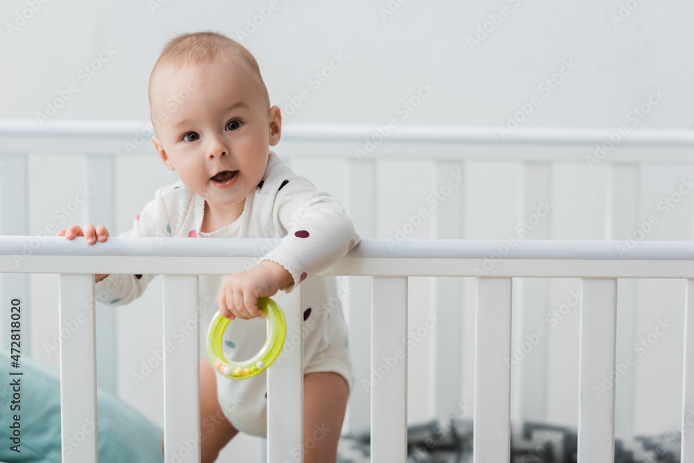 little boy holding rattle ring while standing in crib and looking at camera. little boy holding rattle ring while standing in crib and looking at camera.