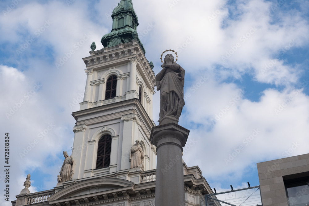 Sculpture of a woman on a pedestal in the image of a saint against the background of the church. Classical european architecture