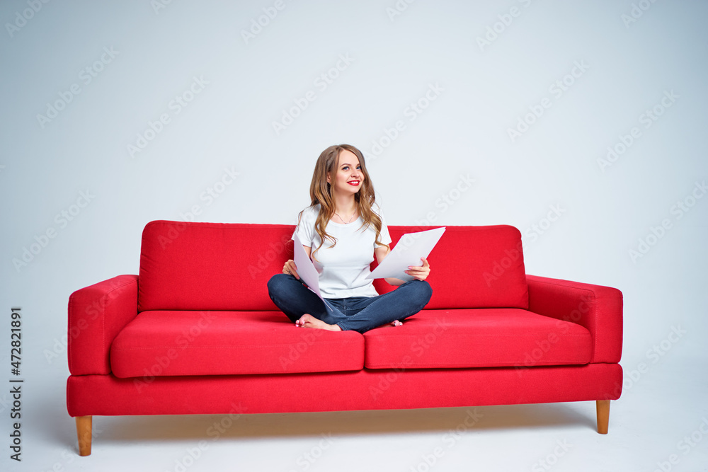 Work and relaxation. Pretty young woman reading documents while sitting on red sofa on white background. Work and relaxation. Pretty young woman reading documents while sitting on red sofa on white background.