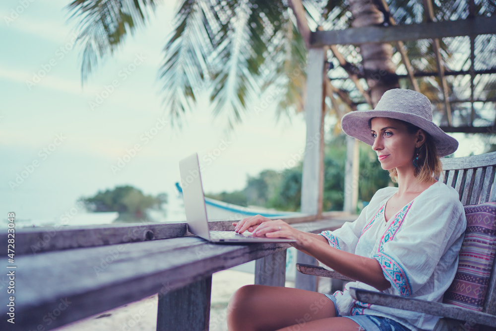 Technology and travel. Working outdoors. Freelance concept. Pretty young woman using laptop in cafe on tropical beach.