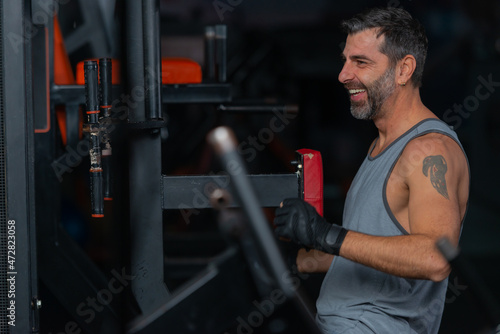 Happy fit mature man sitting and resting between exercises in the gym