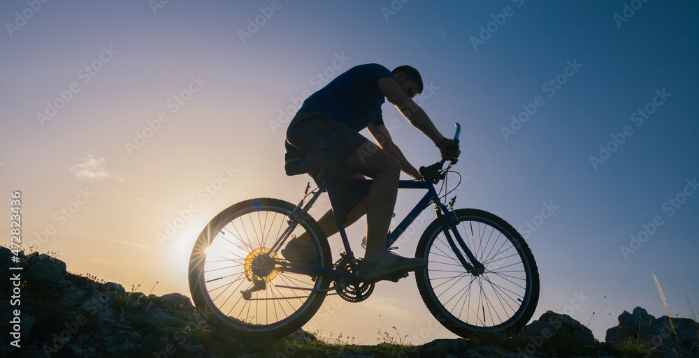 Silhouette of a fit male mountain biker riding his bike uphill on rocky harsh terrain on a sunset. Silhouette of a fit male mountain biker riding his bike uphill on rocky harsh terrain on a sunset.
