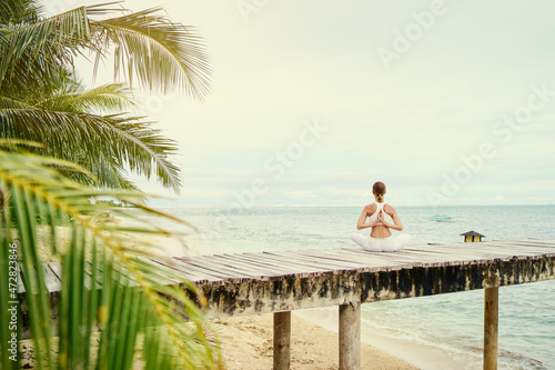 Yoga and meditation. Relaxed young woman in lotus pose on wooden deck with beautiful sea view.