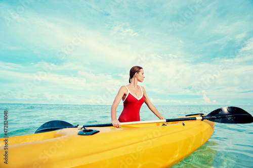 Young woman holding the sea kayak in the tropical calm lagoon.